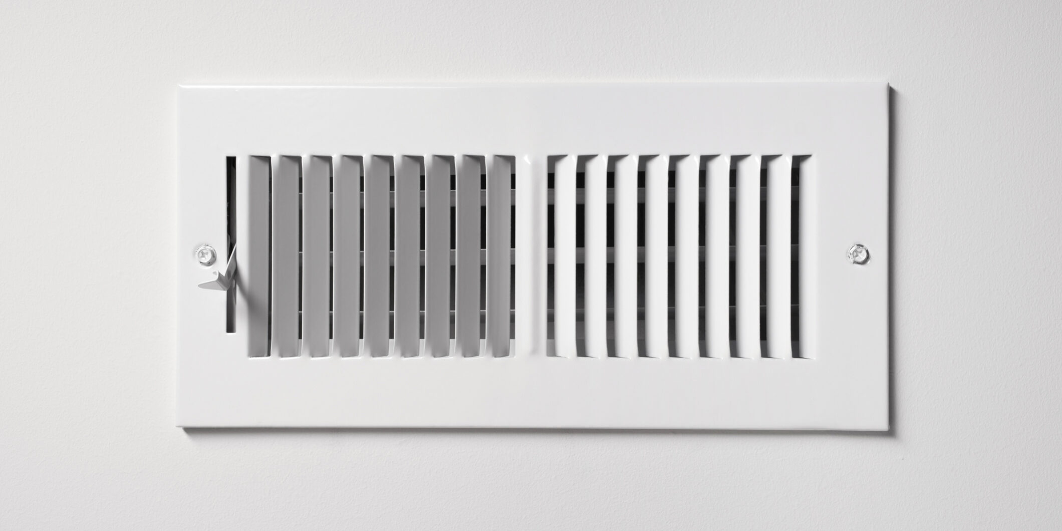 A heating/cooling vent register on the wall of a home, with open/close lever