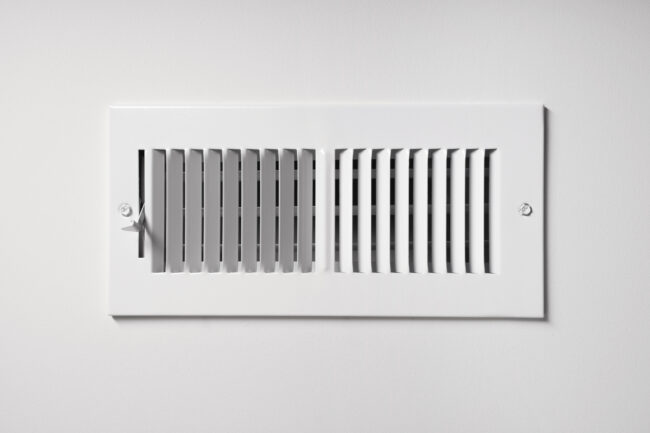 Heating/Cooling Vent A heating/cooling vent register on the wall of a home, with open/close lever