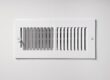 A heating/cooling vent register on the wall of a home, with open/close lever