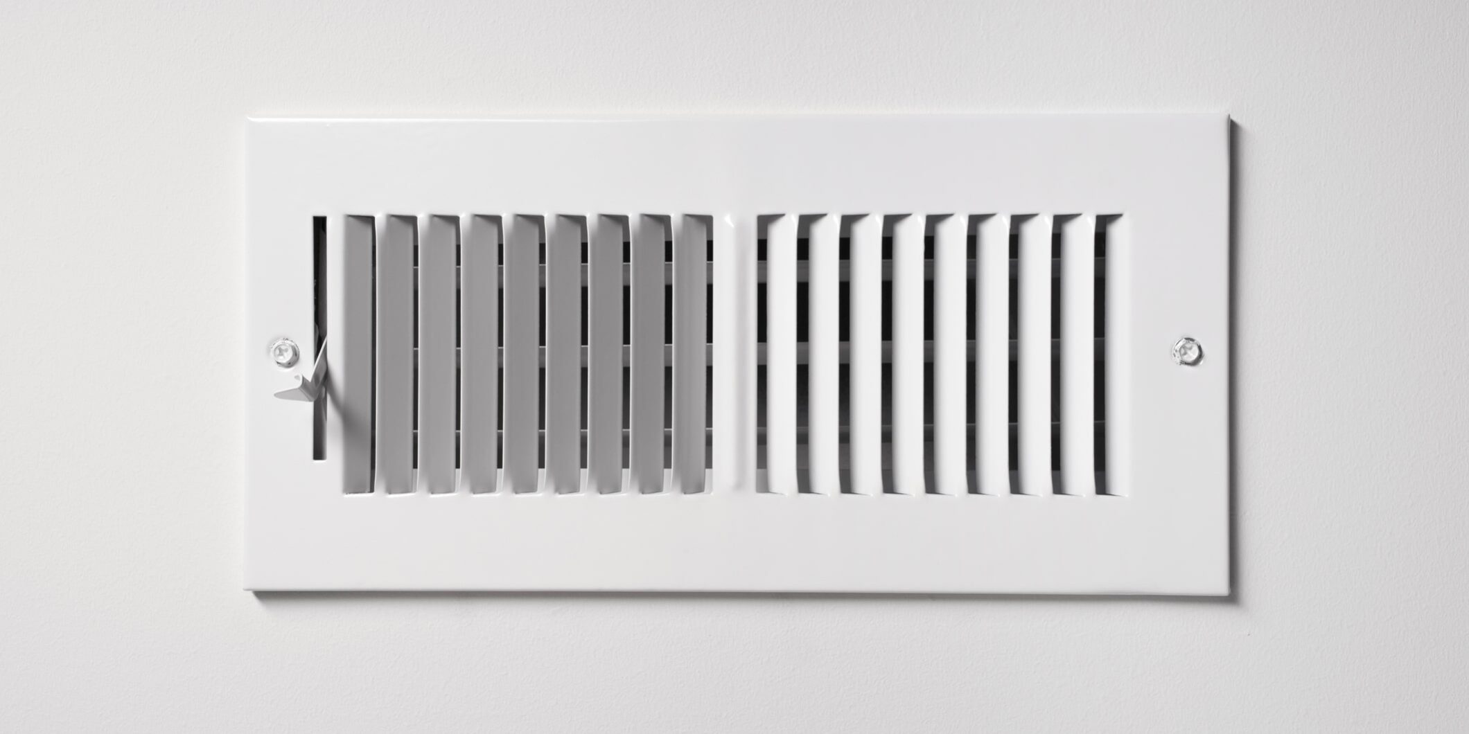 A heating/cooling vent register on the wall of a home, with open/close lever