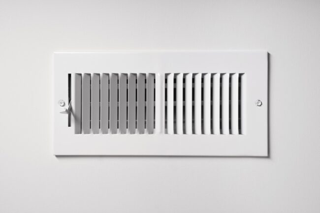 Heating-Cooling-Vent-Stock-Photo-min A heating/cooling vent register on the wall of a home, with open/close lever